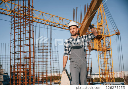 Crane behind. Holding wooden piece. Man is working on the construction site at daytime 126275255