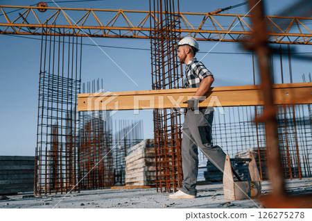 View from the side. Walking and holding wooden plank. Man is working on the construction site at daytime View from the side. Walking and holding wooden plank. Man is working on the construction site at daytime 126275278