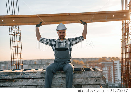Sitting and holding wooden plank. Man is working on the construction site at daytime 126275287