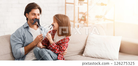 Funny little girl and her dad have mustaches on sticks, posing at home, copy space 126275325