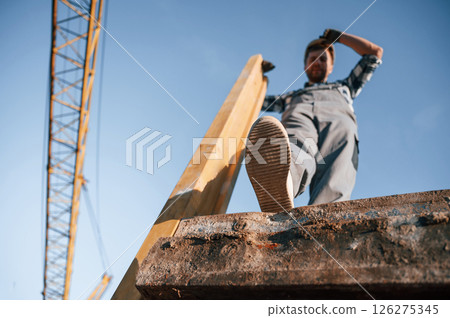 View from below. With big wooden piece. Man is working on the construction site at daytime View from below. With big wooden piece. Man is working on the construction site at daytime 126275345