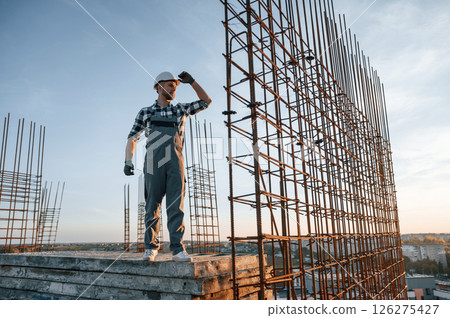 Standing near steel frame. Man is working on the construction site at daytime Standing near steel frame. Man is working on the construction site at daytime 126275427