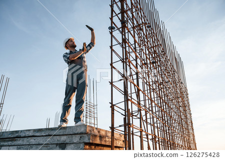 Standing near steel frame. Man is working on the construction site at daytime 126275428