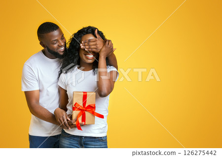 Happy Anniversary, Honey! Attractive Black Man Closing His Woman Eyes, holding gift for her, yellow background Happy Anniversary, Honey! Attractive Black Man Closing His Woman Eyes, holding gift for her, yellow background 126275442