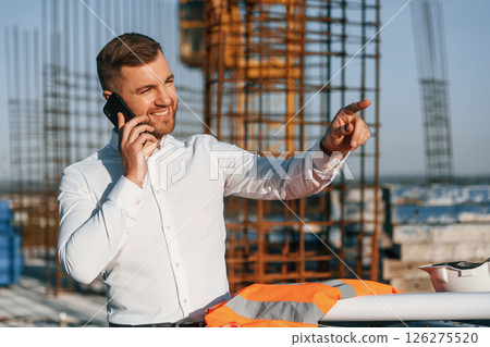 Standing and talking by phone. Businessman in formal clothes is on the construction site at daytime 126275520