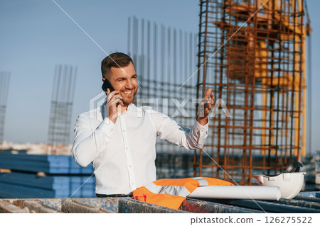 Standing and talking by phone. Businessman in formal clothes is on the construction site at daytime 126275522
