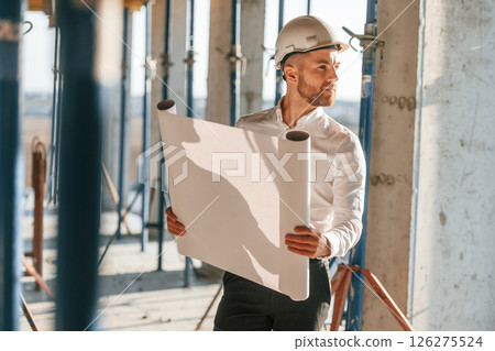 With big paper in hands. Man is working on the construction site at daytime With big paper in hands. Man is working on the construction site at daytime 126275524