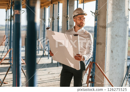 Manager is in the formal clothes. Holding plan in hands. Man is working on the construction site at daytime Manager is in the formal clothes. Holding plan in hands. Man is working on the construction site at daytime 126275525
