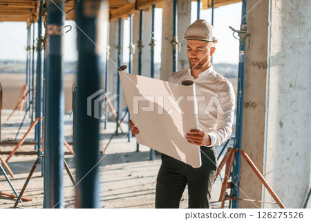 Manager is in the formal clothes. Holding plan in hands. Man is working on the construction site at daytime Manager is in the formal clothes. Holding plan in hands. Man is working on the construction site at daytime 126275526