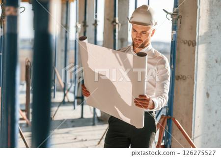 Manager is in the formal clothes. Holding plan in hands. Man is working on the construction site at daytime Manager is in the formal clothes. Holding plan in hands. Man is working on the construction site at daytime 126275527