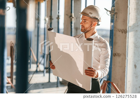 Manager is in the formal clothes. Holding plan in hands. Man is working on the construction site at daytime 126275528