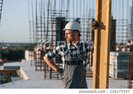 Man is working on the construction site at daytime. Moving the big wooden plank 126275547