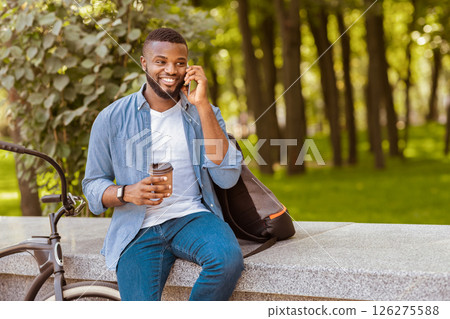 Handsome Afro Guy With Takeout Coffee Sitting On Bench In Park And Talking On Cellphone, Relaxing Outdoors Handsome Afro Guy With Takeout Coffee Sitting On Bench In Park And Talking On Cellphone, Relaxing Outdoors 126275588