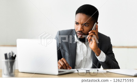 Concerned businessman talking on cell phone and looking at laptop screen, trying to reach technical support to solve issue with his computer, panorama 126275593