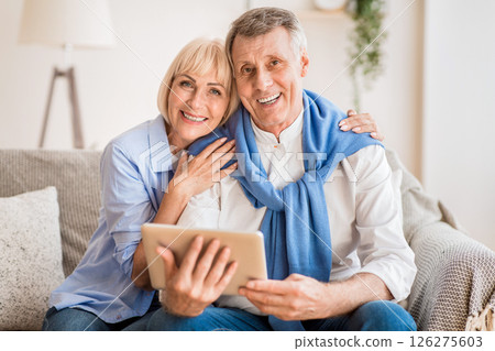 Excited mature couple with digital tablet smiling to camera, woman embracing husband 126275603