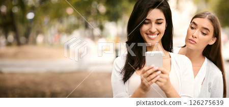Jealous Friend. Envious Girl Peeking At Girlfriend's Phone While She Texting Walking Together Outdoors Jealous Friend. Envious Girl Peeking At Girlfriend's Phone While She Texting Walking Together Outdoors 126275639
