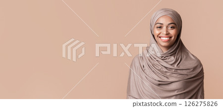 Portrait of modest black muslim girl in hijab smiling at camera, posing over yellow background, empty space 126275826