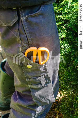 Bright orange scissors in work pants pocket in garden, sunny outdoor setting. High quality photo 126275949