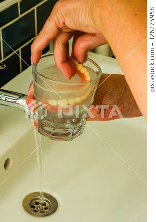 Dentures in a clear glass of water under faucet, dental hygiene concept. High quality photo Dentures in a clear glass of water under faucet, dental hygiene concept. High quality photo 126275958