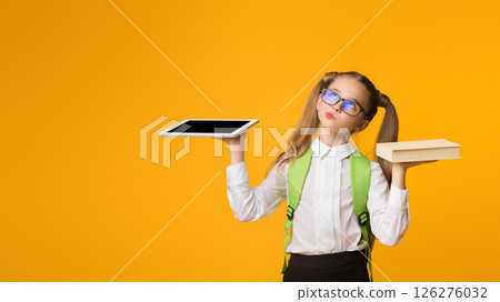 Books Or Gadgets. Nurdy School Girl Comparing Schoolbook And Digital Tablet Over Yellow Background. Empty Space Books Or Gadgets. Nurdy School Girl Comparing Schoolbook And Digital Tablet Over Yellow Background. Empty Space 126276032