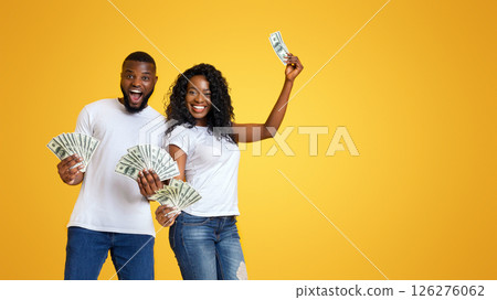 Excited black couple holding dollars in both hands, yellow studio background 126276062