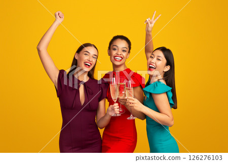 Glamour Party. Three Girls Models In Evening Dresses Clinking Glasses Having Fun Celebrating Something Standing Over Yellow Background Glamour Party. Three Girls Models In Evening Dresses Clinking Glasses Having Fun Celebrating Something Standing Over Yellow Background 126276103