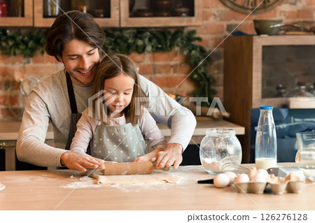 Cute little girl and her father in aprons rolling out the dough together on kitchen table, making cookies, free space 126276128