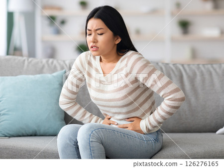 Stomach Ache. Sick Asian Woman Suffering From Acute Abdominal Pain At Home, Upset Korean Female Having Menstrual Pain Or Problems With Digestion, Sitting On Couch And Touching Belly, Free Space 126276165