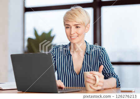 Happy Businesswoman At Laptop Working Browsing Internet Holding Coffee Cup Sitting In Modern Office. Selective Focus Happy Businesswoman At Laptop Working Browsing Internet Holding Coffee Cup Sitting In Modern Office. Selective Focus 126276213