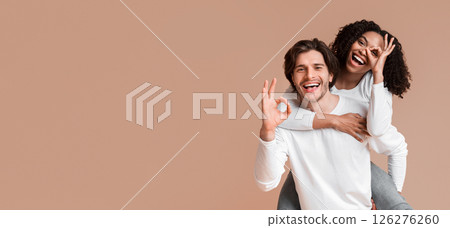 Everything is ok. Happy multiracial couple showing okay gesture while having fun together over yellow background, guy piggybacking his afro girlfriend Everything is ok. Happy multiracial couple showing okay gesture while having fun together over yellow background, guy piggybacking his afro girlfriend 126276260