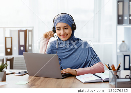 Foreign Languages Online Concept. Portrait Of Smiling Arabic Girl In Hijab And Headset Watching Webinar On Laptop While Sitting In Office 126276285