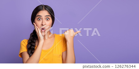 Omg, Cool Offer. Surprised young indian lady pointing at free space isolated over purple studio background. Excited shocked woman showing copy space and place for advert or promotional text, banner 126276344