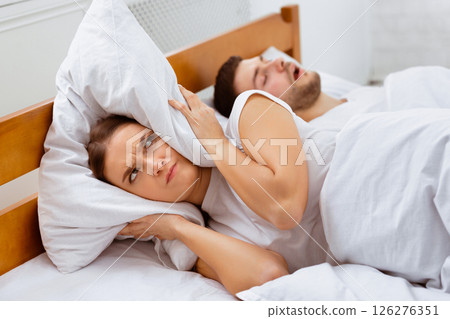 Snoring. Angry Girlfriend Covering Ears With Pillow Lying Near Sleeping Boyfriend In Bed At Home. Selective Focus Snoring. Angry Girlfriend Covering Ears With Pillow Lying Near Sleeping Boyfriend In Bed At Home. Selective Focus 126276351