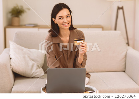 Easy Money Transfer. Happy young woman holding credit card, sitting on couch and looking at camera, copyspace 126276364