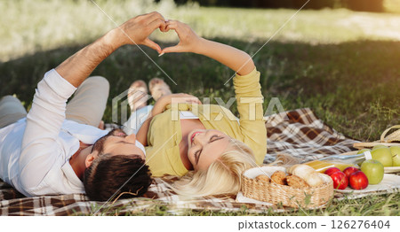Happy couple in love enjoying day together, lying on plaid in park, making heart symbol Happy couple in love enjoying day together, lying on plaid in park, making heart symbol 126276404