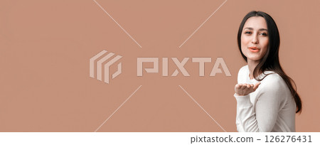 Beautiful brunette girl blowing a kiss at camera, flirting with someone, posing over yellow background, free space 126276431