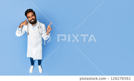 A smiling Indian doctor with a beard is wearing a white coat and stethoscope. He is gesturing with his hands, making a call gesture with his left hand and pointing at copy space A smiling Indian doctor with a beard is wearing a white coat and stethoscope. He is gesturing with his hands, making a call gesture with his left hand and pointing at copy space 126276561