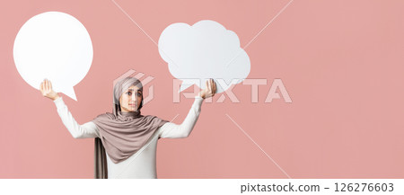 Difficult choice. Muslim girl in hijab holding two empty speech bubbles over pink background, free space 126276603