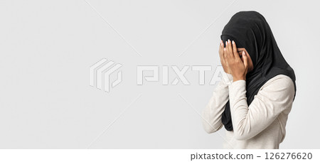 Violence against muslims concept. Upset black woman in hijab covering face with hands, crying over gray background, free space Violence against muslims concept. Upset black woman in hijab covering face with hands, crying over gray background, free space 126276620