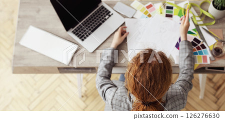 Designer At Work. Top view of red-haired dressmaker drawing sketches, sitting at table, instructing, copy space 126276630