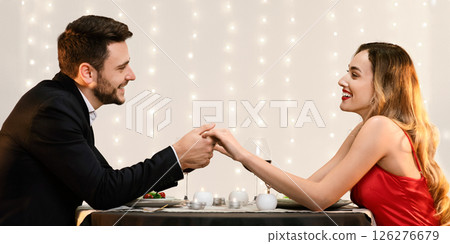Romantic couple holding hands, celebrating their anniversary on date in restaurant, looking at each other with love and affection, side view Romantic couple holding hands, celebrating their anniversary on date in restaurant, looking at each other with love and affection, side view 126276679