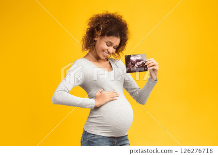 First sonography. Future mother holding ultrasound scan and touching her belly, pink background First sonography. Future mother holding ultrasound scan and touching her belly, pink background 126276718