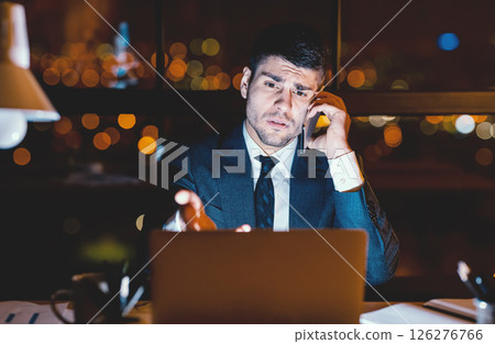 Displeased Businessman Calling To Technical Support Complaining About Problems With Laptop Sitting In Modern Office At Night. Low Light 126276766