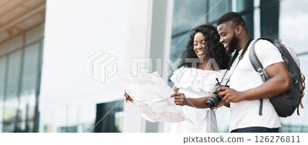 Black couple in casual clothes stands in front of a modern building, looking at a map, presumably planning their day exploring the city, copy space 126276811