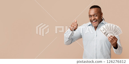 Excited middle aged afro man enjoying big jackpot, showing thumb up with lots of money, orange studio background Excited middle aged afro man enjoying big jackpot, showing thumb up with lots of money, orange studio background 126276812