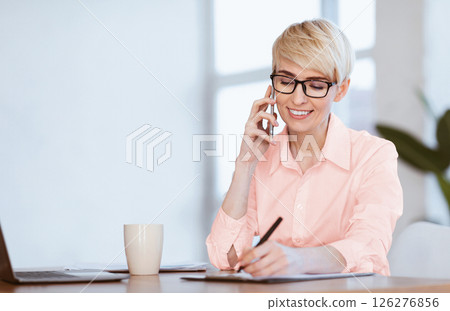 Entrepreneur Lady Talking On Phone Taking Notes Making Business Schedule Sitting At Workplace Indoors. Selective Focus, Free Space 126276856