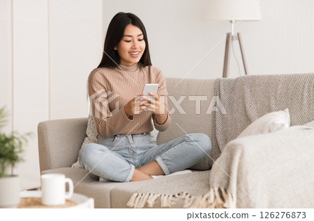 Weekend at home. Girl checking social networks on smartphone, resting on sofa Weekend at home. Girl checking social networks on smartphone, resting on sofa 126276873