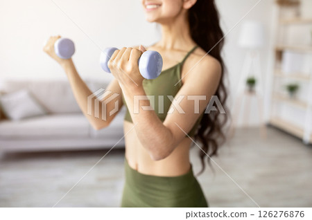 Closeup of young Indian lady exercising with dumbbells at home during covid quarantine, selective focus. Unrecognizable Asian woman strengthening her arm muscles, having domestic strength training Closeup of young Indian lady exercising with dumbbells at home during covid quarantine, selective focus. Unrecognizable Asian woman strengthening her arm muscles, having domestic strength training 126276876