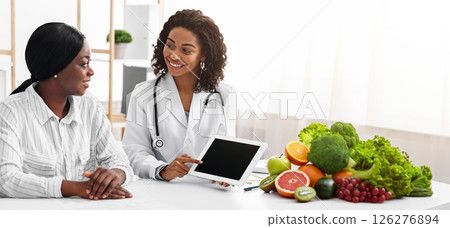 Friendly female dietologist showing black lady patient empty digital tablet screen in her office, technologies in medical care 126276894