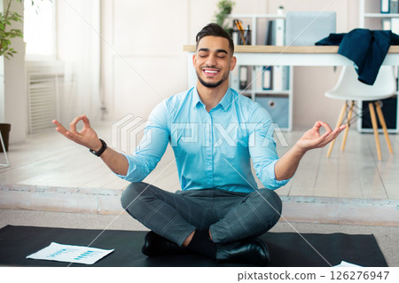 Workplace stress management concept. Calm Arab man meditating with closed eyes at modern office. Young businessman feeling peaceful and balanced, doing yoga on mat 126276947
